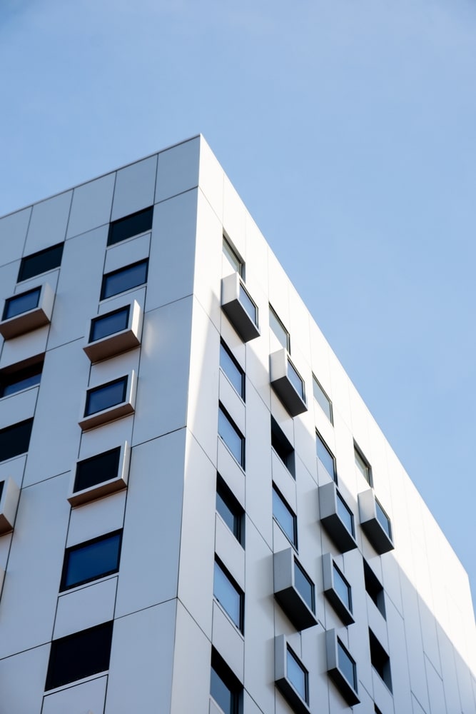 Architecture moderne : façade blanche géométrique et ciel bleu. Façade angulaire blanche d'un bâtiment moderne minimaliste. Contre-plongée montrant des fenêtres carrées encadrées et des ombres nettes sous un ciel bleu.