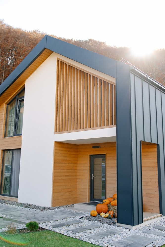 Maison moderne : Bois clair, blanc et architecture contemporaine. Architecture moderne en bois clair et métal gris foncé. Façade blanche, grand écran de lattes verticales. Sentier en pierre, citrouilles d'automne à l'entrée.
