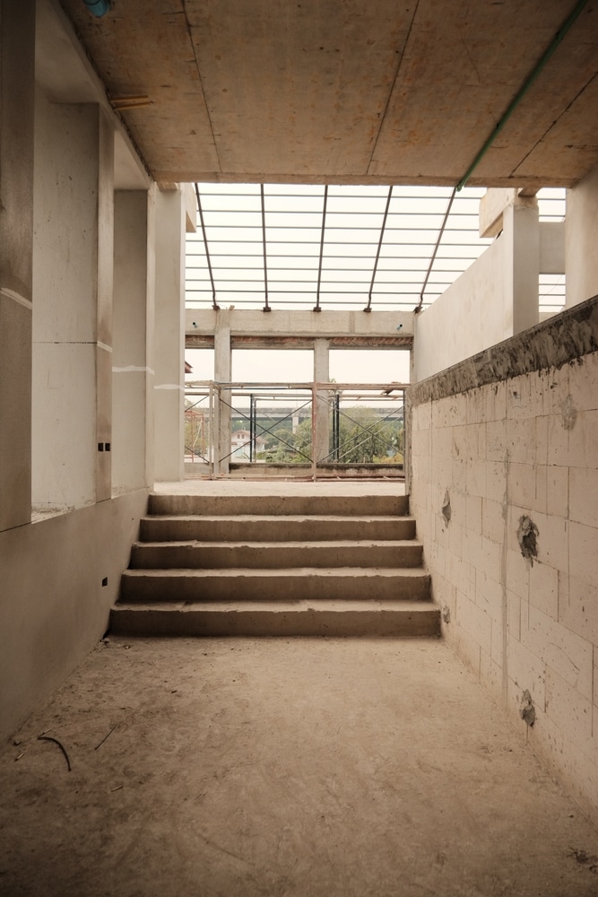 Construction : Escalier en béton brut du chantier inachevé. Escalier en béton brut sur un chantier inachevé. Les cinq marches mènent à une ouverture avec une charpente métallique et une vue extérieure.