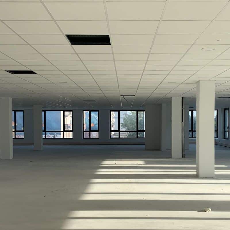 Plateau de bureaux vide en travaux : espace commercial lumineux. Plateau de bureaux commercial vide sous faux plafond, en attente d'aménagement. Les rayons de soleil projettent de longues ombres sur le sol.